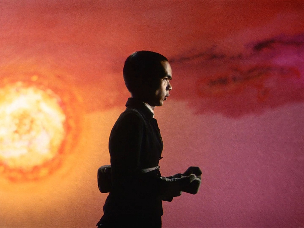 Rokuchan walking past a vivid apocalyptic sun, illustrating Kurosawa's use of color and Noh-inspired visual symbolism in Dodes'ka-den.