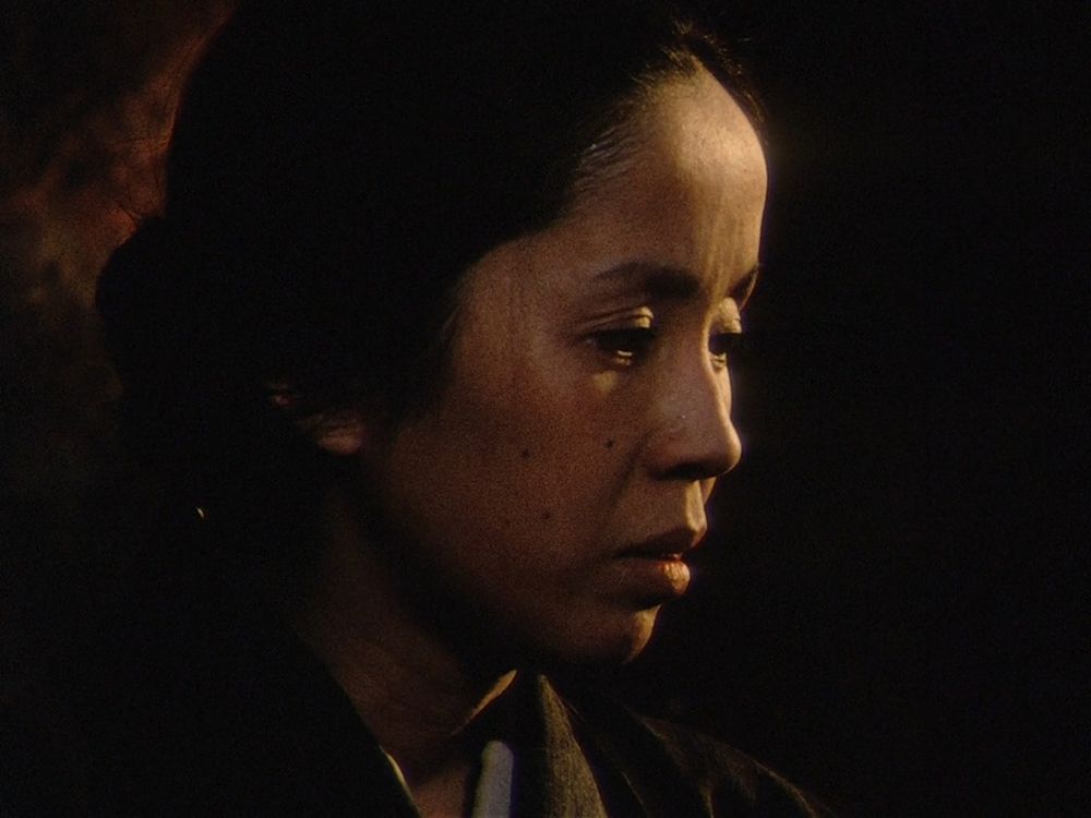Ocho, Mr. Hei's estranged wife, shown in profile in a dimly lit scene from Dodes'ka-den.