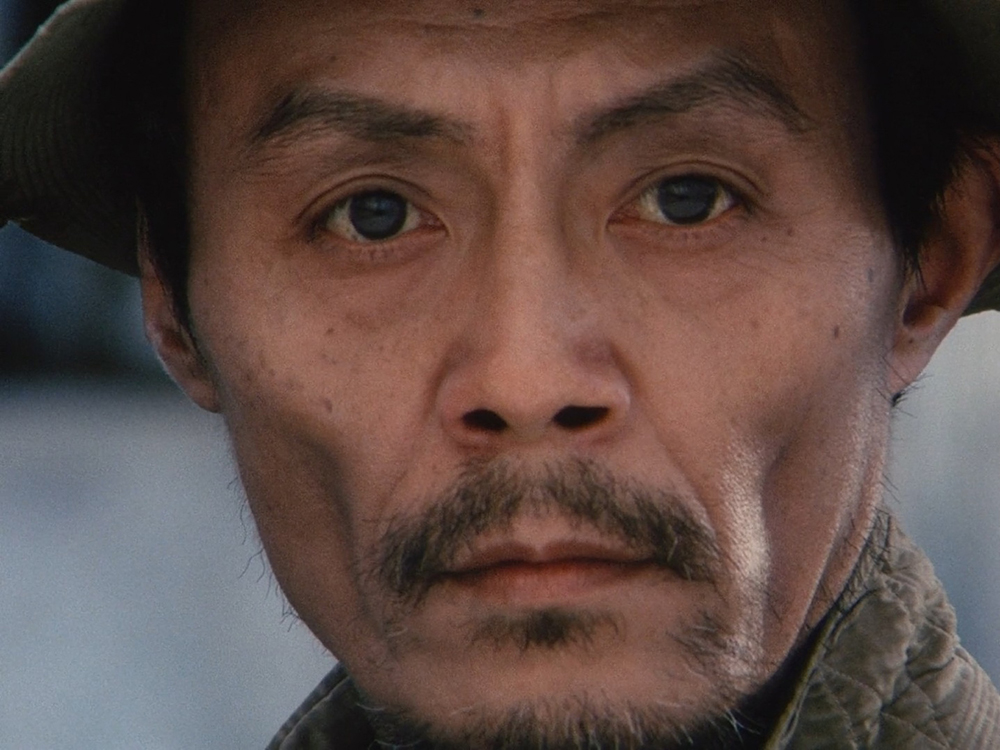Close-up of Mr. Hei's expressionless face from Dodes'ka-den, emphasizing his emotional isolation.
