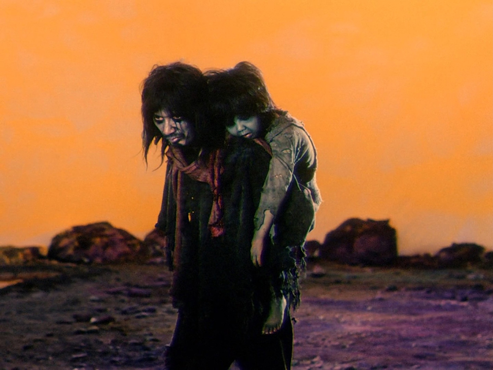 Father carrying Son across a barren landscape in Dodes'ka-den, illustrating their poverty and isolation.