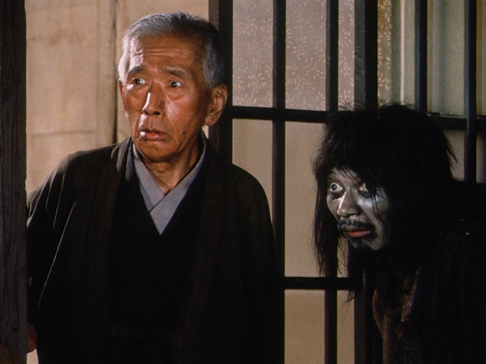 Mr. Tanba standing beside Father, whose appearance resembles a traditional Noh demon figure.